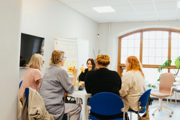 Viisi ihmistä istuu työpaikan pöydän ääressä.