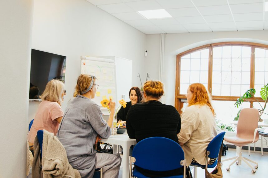 Viisi ihmistä istuu työpaikan pöydän ääressä.