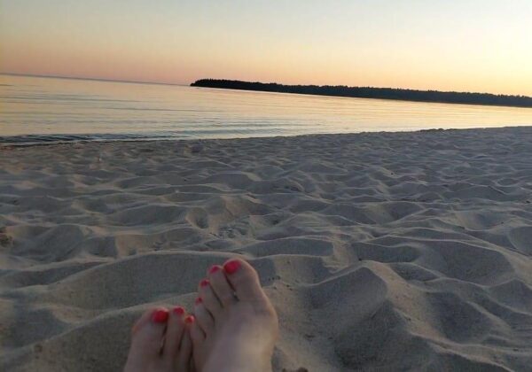 Lakatut varpaankynnet hiekkarannalla meren äärellä auringonlaskun aikaan.