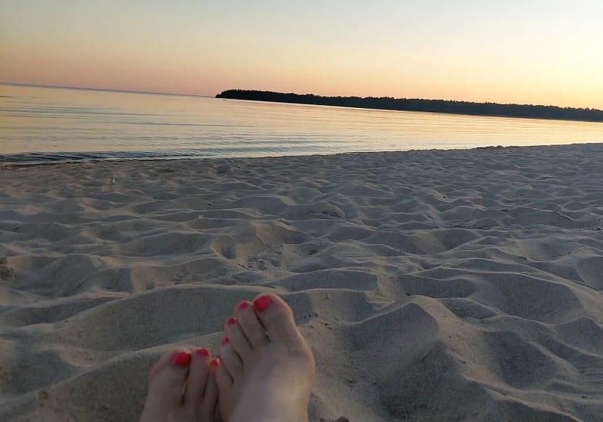 Lakatut varpaankynnet hiekkarannalla meren äärellä auringonlaskun aikaan.