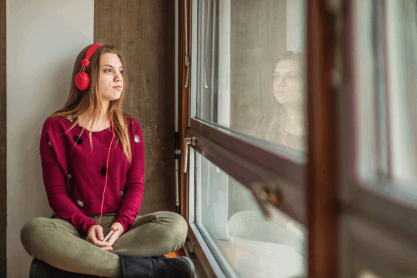 Nuori istuu kuulokkeet korvilla ikkunan ääressä ulos katsoen.