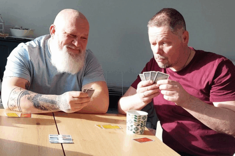 Kaksi miestä istuu pöydän ääressä pelaamassa korttia.