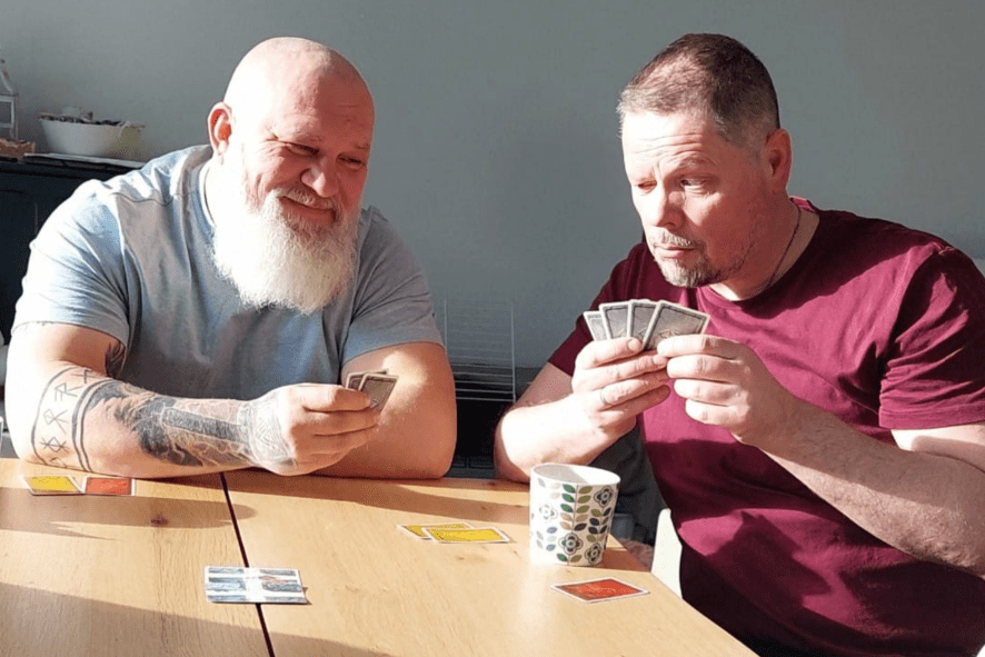 Kaksi miestä istuu pöydän ääressä pelaamassa korttia.